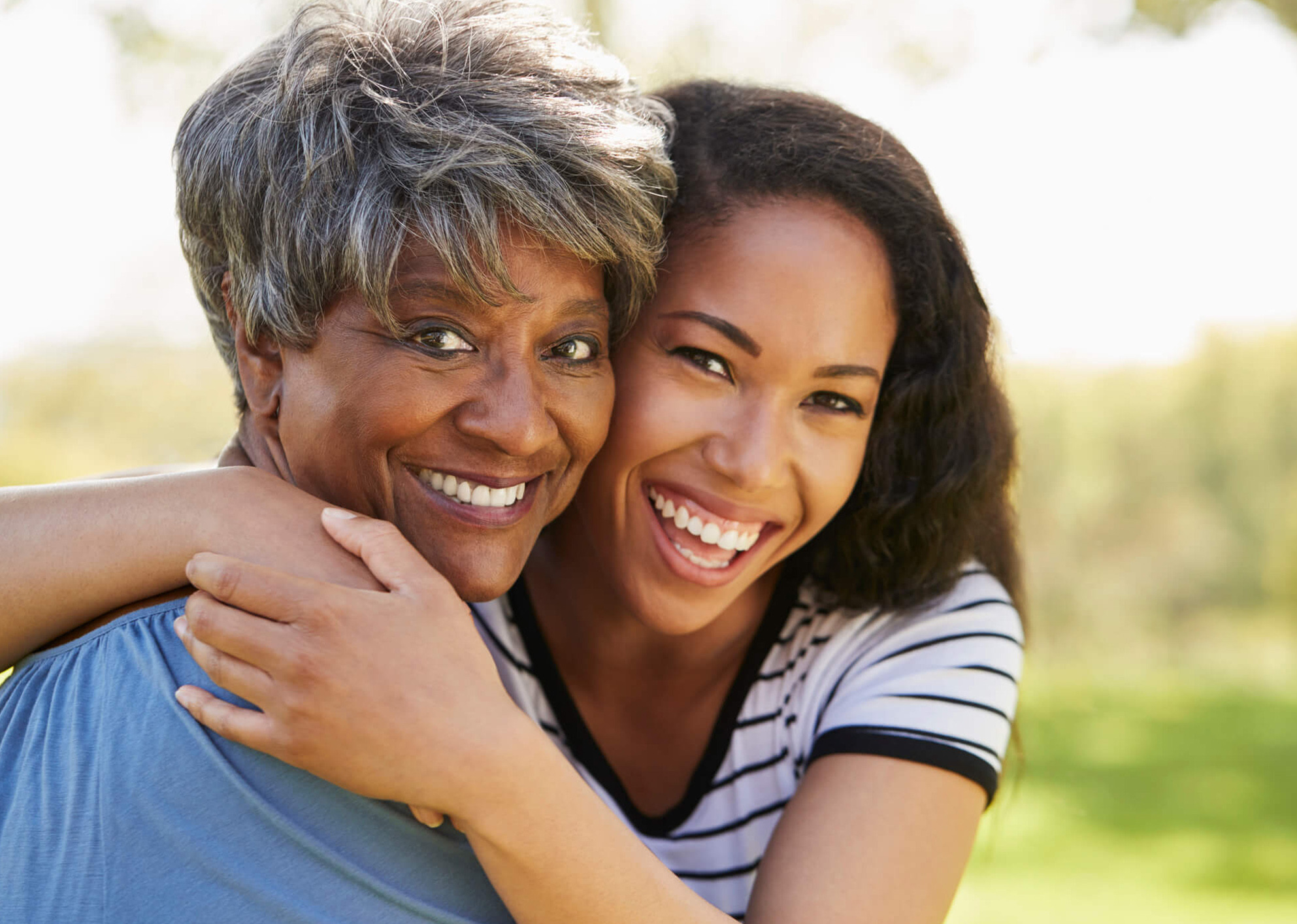 young african american adult hugging and smiling with an older african american lady with grey hair